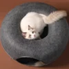 A contented white cat with brown spots lounges inside a dark grey wool felt cat tunnel, exuding coziness and comfort.