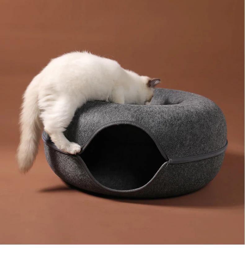 Playful white cat with brown patches diving into a dark grey wool felt tunnel bed, embodying fun and curiosity.